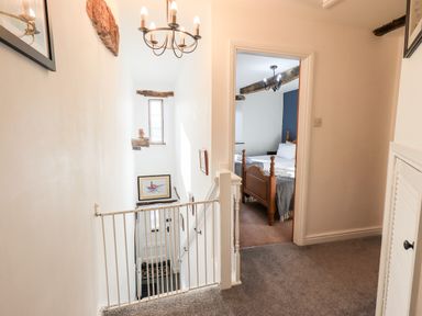 A hallway with a baby gate at the top of stairs and a bedroom visible at the end at St Peters Cottage in Milnthorpe