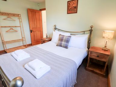 A bedroom with a double bed pillows bedside tables a lamp an open wooden door and a wooden clothes rack at St Peters Cottage in Milnthorpe