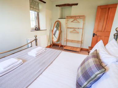 A bedroom with a made bed a standing mirror a wooden clothes rack and a window at St Peters Cottage Milnthorpe