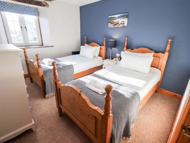 A bedroom with two single wooden beds a bedside table with a lamp and teddy bear and a window with a patterned blind at St Peters Cottage in Milnthorpe