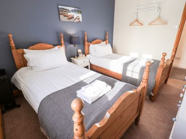 A bedroom with two single wooden beds a nightstand with a lamp and a teddy bear and wall hooks with hangers at St Peters Cottage in Milnthorpe