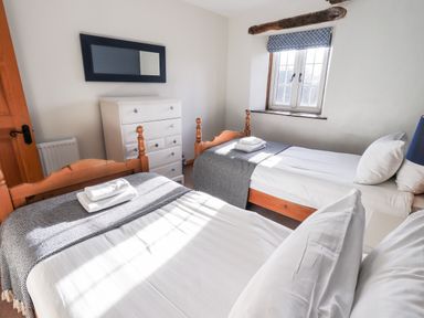 A bedroom with two single beds a white chest of drawers a mirror and a window with a blue patterned blind at St Peters Cottage Milnthorpe