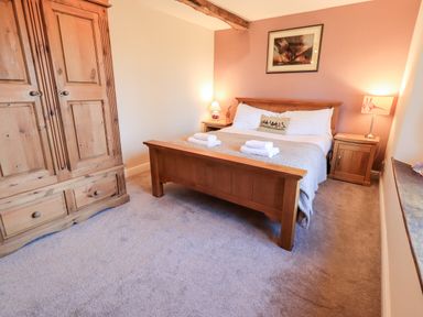 A bedroom with a wooden bed, wardrobe, two bedside tables with lamps and a framed picture on the wall at St Peters Cottage in Milnthorpe