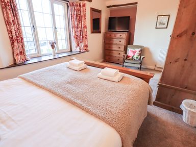 A bedroom with a bed covered in blankets and towels near a window with red curtains and a dresser with a TV at St Peters Cottage in Milnthorpe