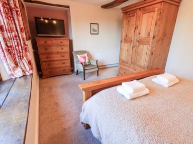 A bedroom with a wooden bed frame covered with towels a wooden wardrobe a chest of drawers with a TV and an armchair at St Peters Cottage Milnthorpe
