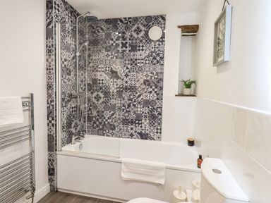 A bathroom with a bathtub shower combination patterned tiles on the wall towel rail and a toilet at St Peters Cottage in Milnthorpe