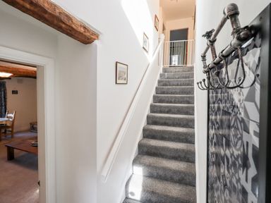 A stairway with a baby gate at the top and a metal coat rack on the wall at St Peters Cottage in Milnthorpe
