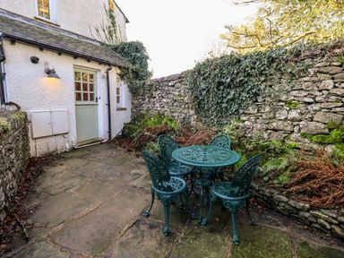 A stone patio with green metal table and four chairs next to a stone wall covered with ivy at St Peters Cottage in Milnthorpe