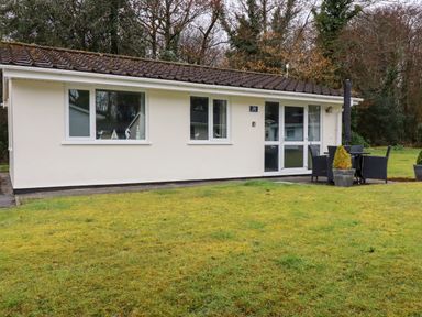 A small cream-colored cottage with three windows and a glass door with outdoor table and chairs on the lawn at Blue Sky Cottage in Rosecraddoc Lodge near Liskeard
