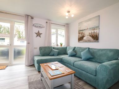 A living room with a blue-green corner sofa a wooden coffee table and a beach painting at Blue Sky Cottage Rosecraddoc Lodge near Liskeard