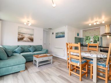 A living room with a green sectional sofa a wooden coffee table a dining table with chairs and a kitchen area at Blue Sky Cottage Rosecraddoc Lodge near Liskeard
