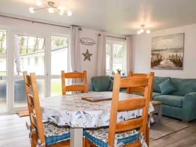 A dining area with wooden chairs around a table and a living room with a green sofa and wall art at Blue Sky Cottage Rosecraddoc Lodge near Liskeard