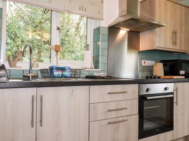 A kitchen with a stainless steel oven and stove a sink with a faucet and drying rack wooden cabinets and drawers and a window with a nature view at Blue Sky Cottage Rosecraddoc Lodge near Liskeard
