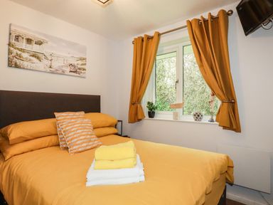 A bedroom with a bed with yellow bedding and pillows a window with curtains and a TV mounted on the wall at Blue Sky Cottage Rosecraddoc Lodge near Liskeard