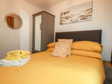A bedroom with a bed with yellow bedding and stacked towels on it a wardrobe with a mirror and a round wall mirror at Blue Sky Cottage Rosecraddoc Lodge near Liskeard