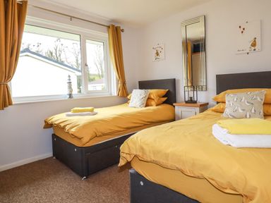 A bedroom with two single beds with yellow bedding a window with yellow curtains and a small nightstand with a lamp at Blue Sky Cottage Rosecraddoc Lodge near Liskeard