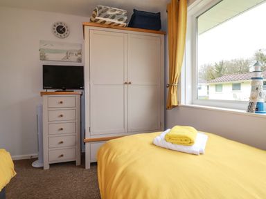A bedroom with a wardrobe a chest of drawers a TV and a bed with yellow bedding at Blue Sky Cottage Rosecraddoc Lodge near Liskeard