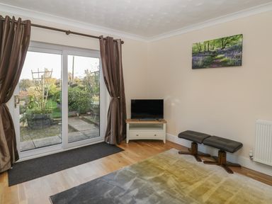 A room with a sliding glass door with curtains a small television on a stand two stools and a rug on a wooden floor at The Annex in Drybrook