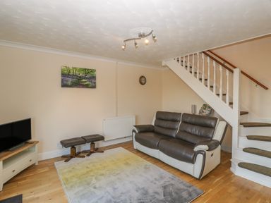 A living room with a sofa two stools a carpet television under stairs and a wall clock at The Annex in Drybrook