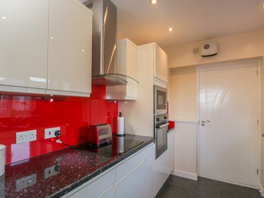 A kitchen with white cabinets a black countertop a red toaster and red backsplash at The Annex in Drybrook
