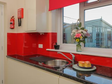 A kitchen countertop with a sink vase of flowers and cakes on plates by a window at The Annex in Drybrook
