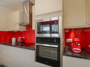A kitchen with a red toaster, red coffee machine, microwave, oven, hood and white cabinets at The Annex in Drybrook
