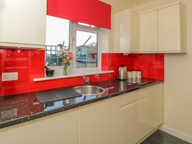 A kitchen with cream cabinets red backsplash and countertop with a sink electric kettle and canisters at The Annex in Drybrook