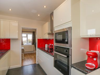 A kitchen with white cabinets red backsplash and black countertop with a microwave oven and coffee machine at The Annex in Drybrook
