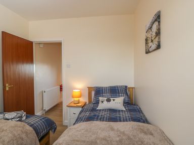 A bedroom with two single beds a nightstand with a lamp an open door and a picture of kittens at The Annex in Drybrook