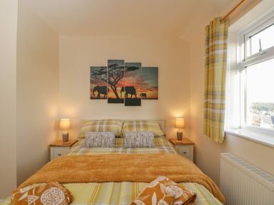 A bedroom with a bed and bedside tables with lamps and a window with yellow plaid curtains at The Annex in Drybrook