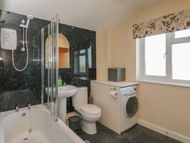 A bathroom with a bathtub shower toilet sink washing machine and window at The Annex in Drybrook