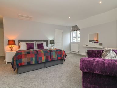 A bedroom with a bed covered with a colorful blanket bedside tables lamps a window and a purple sofa at The Old Coach House in Braunton