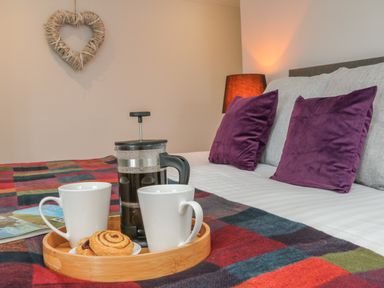 A bed with purple pillows and a tray holding a coffee press and two cups on a plaid blanket at The Old Coach House in Braunton