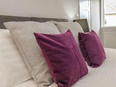 A bed with two gray pillows and two purple cushions at The Old Coach House in Braunton