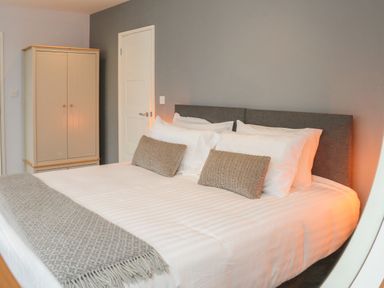 A bedroom with a large bed white bedding two grey pillows and a grey blanket next to a wardrobe at The Old Coach House in Braunton