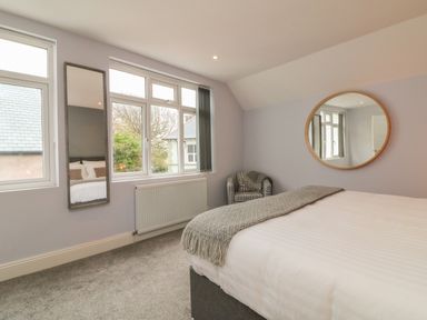 A bedroom with a bed a round mirror a window and a plaid upholstered chair at The Old Coach House in Braunton