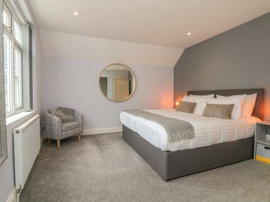 A bedroom with a double bed two pillows a plaid armchair and a round mirror on the wall at The Old Coach House in Braunton