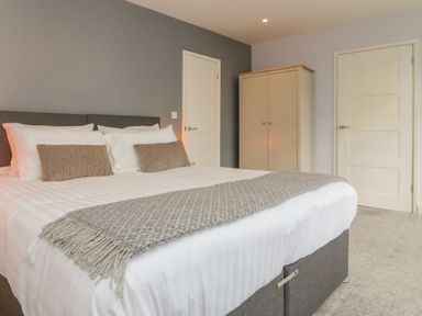 A bedroom with a double bed two pillows two cushions a beige throw a wardrobe and two doors at The Old Coach House in Braunton