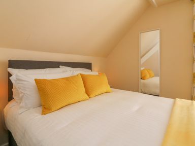 A bedroom with a double bed with white linens and yellow pillows with a full-length mirror on the wall at The Old Coach House in Braunton