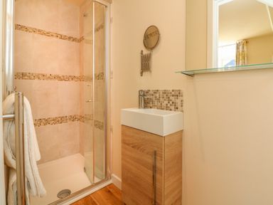A bathroom with a shower enclosure a sink with wooden cabinet and a mirror at The Old Coach House in Braunton
