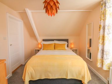 A bedroom with a bed yellow cushions and a blanket bedside tables with lamps a mirror and floral curtains at The Old Coach House in Braunton