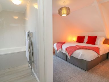 A bedroom with a bed with red pillows and blankets adjacent to a bathroom with a bathtub and towel rack at The Old Coach House in Braunton