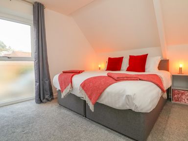 A bedroom with a double bed red throw blankets and pillows bedside tables and gray curtains at The Old Coach House in Braunton