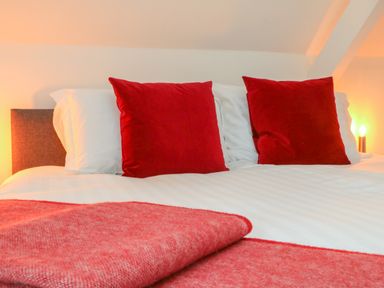 A bed with white sheets and red pillows and a red blanket at The Old Coach House in Braunton