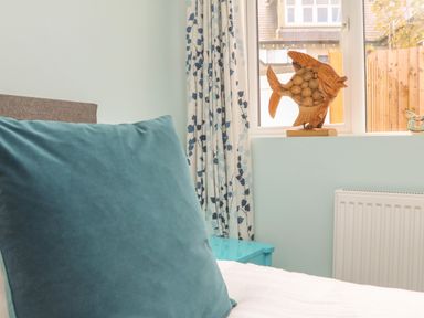 A pillow on a bed near a window with curtains and wooden fish decoration at The Old Coach House in Braunton