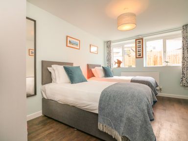 A bedroom with two single beds with blue pillows and gray throws near windows at The Old Coach House in Braunton