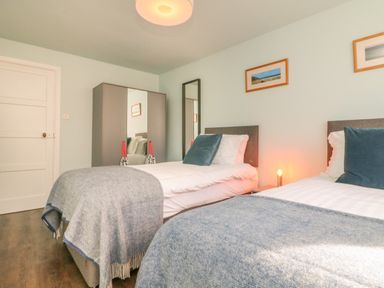 A bedroom with two single beds a wardrobe a mirror and framed pictures on the wall at The Old Coach House in Braunton