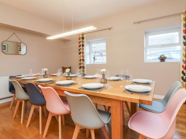 A dining room with a wooden table set with plates glasses and cutlery surrounded by mixed color chairs at The Old Coach House in Braunton
