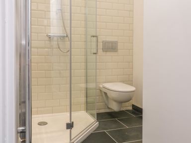 A bathroom with a glass shower enclosure and a wall-mounted toilet at The Old Coach House in Braunton