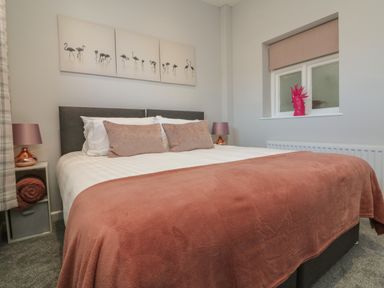 A bedroom with a bed with pink pillows and blanket a window with a pink blind and a bedside table with a lamp at The Old Coach House in Braunton